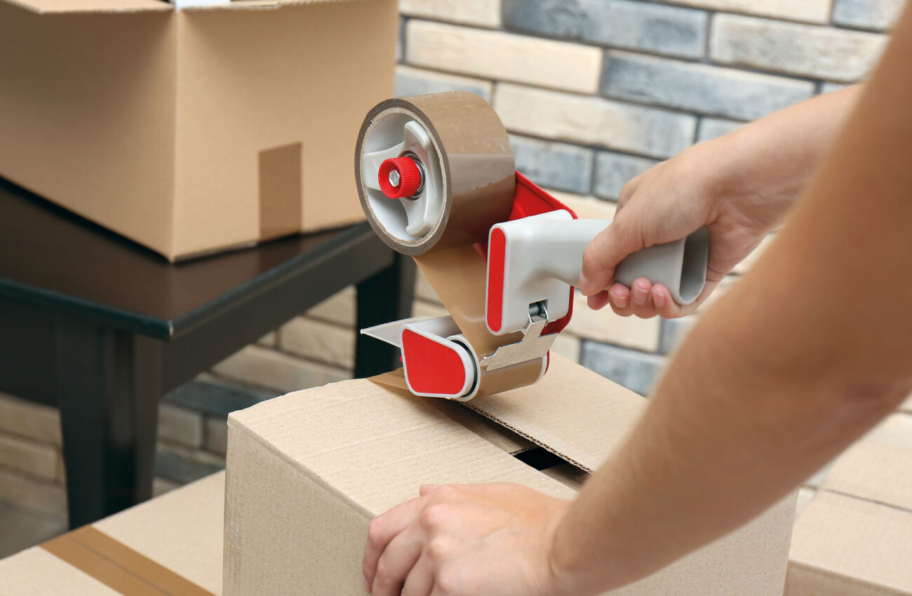 Woman packing carton box indoors, closeup. Moving day