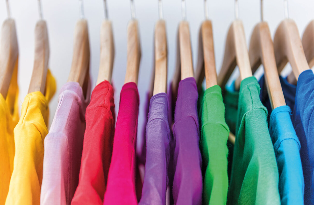 Fashion clothes on clothing rack   bright colorful closet. Closeup of rainbow color choice of trendy female wear on hangers in store closet or spring cleaning concept. Summer home wardrobe.